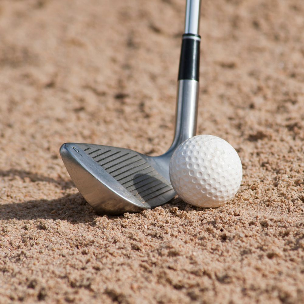 A golfer hitting a golf ball with a sand wedge